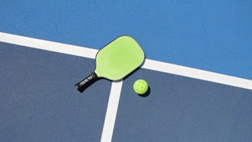 A pickleball paddle and ball on a court. A pickleball paddle and ball on a court.
