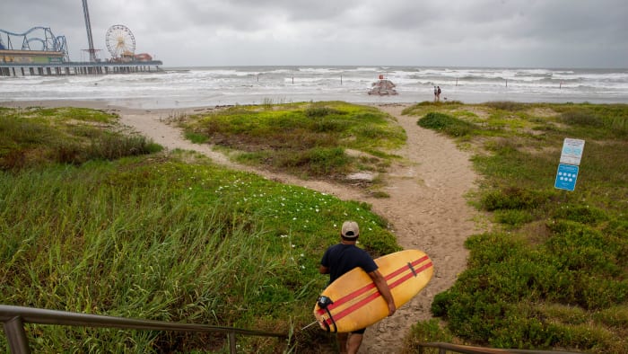 A surfer walks down to the beach on Wednesday, Aug. 25, 2020, near Galveston Island Historic Pleasure Pier.