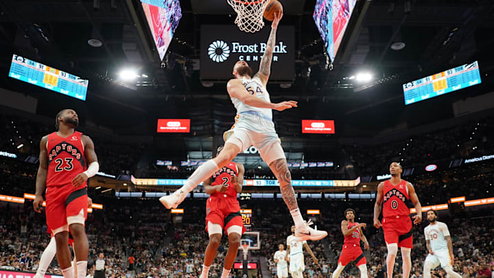 Apr 13, 2025; San Antonio, Texas, USA; San Antonio Spurs forward Sandro Mamukelashvili (54) drives to the basket past Toronto Raptors guards Jamal Shead (23), AJ Lawson (0), and forward Jonathan Mogbo (2) during the second half at Frost Bank Center. Mandatory Credit: Scott Wachter-Imagn Images