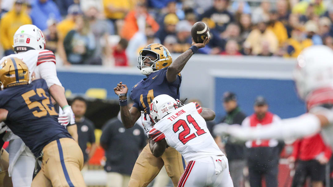 Sep 27, 2025; Morgantown, West Virginia, USA; West Virginia Mountaineers quarterback Khalil Wilkins (14) throws a pass while hit by Utah Utes safety Nate Tilmon (21) during the third quarter at Milan Puskar Stadium. Mandatory Credit: Ben Queen-Imagn Images