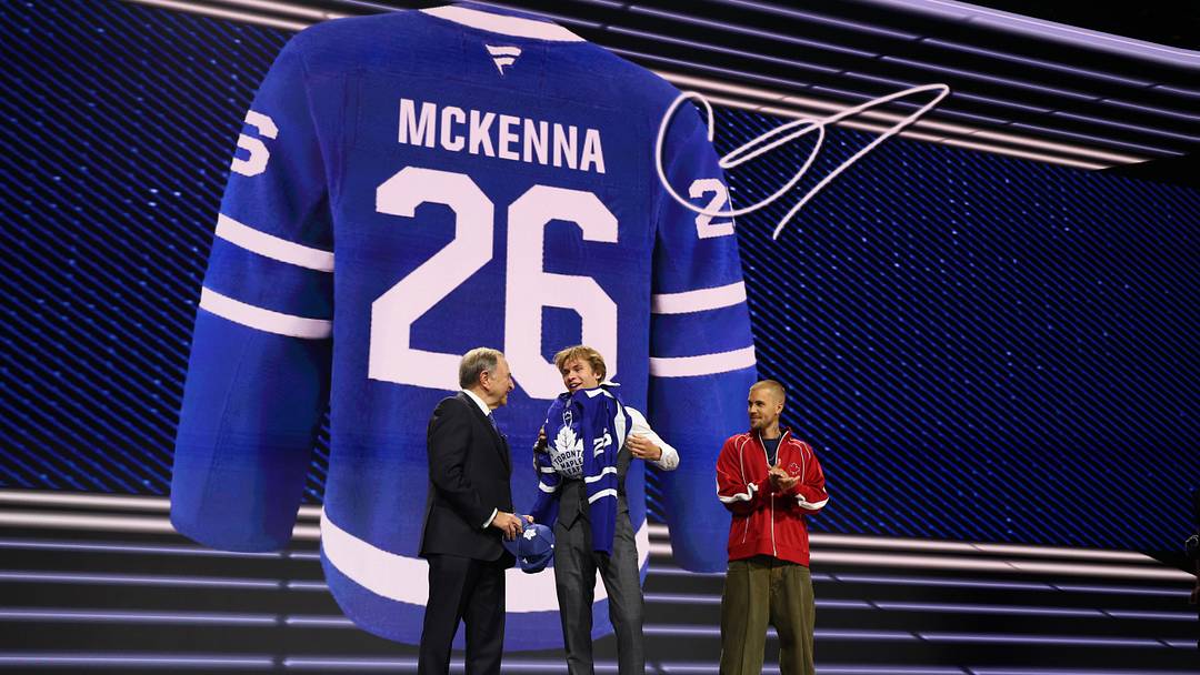 Jun 26, 2026; Buffalo, New York, USA; Gavin McKenna puts on a sweater beside NHL commissioner Gary Bettman and singer Justin Bieber after being selected with the first pick in the first round of the 2026 NHL Draft by the Toronto Maple Leafs at KeyBank Center. Mandatory Credit: Timothy T. Ludwig-Imagn Images