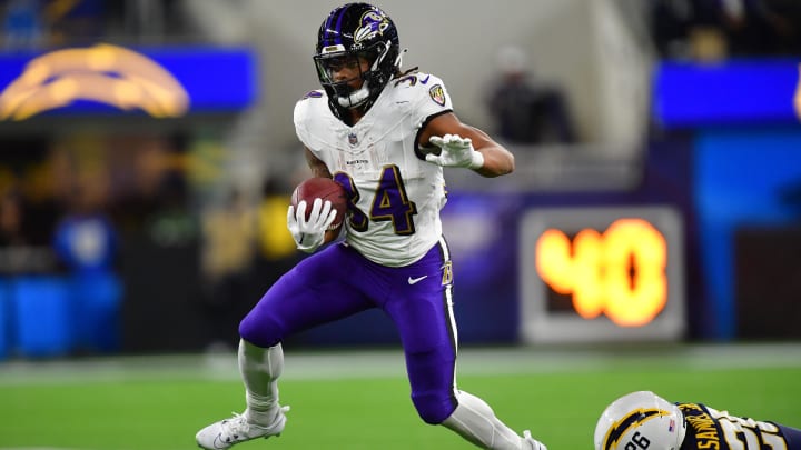 Nov 26, 2023; Inglewood, California, USA; Baltimore Ravens running back Keaton Mitchell (34) runs the ball ahead of Los Angeles Chargers cornerback Asante Samuel Jr. (26) during the first half at SoFi Stadium. Mandatory Credit: Gary A. Vasquez-USA TODAY Sports