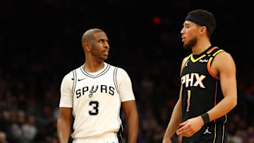 Dec 3, 2024; Phoenix, Arizona, USA; San Antonio Spurs guard Chris Paul (3) talks to Phoenix Suns guard Devin Booker (1) in the second half of an NBA Cup game at Footprint Center. Mandatory Credit: Mark J. Rebilas-Imagn Images