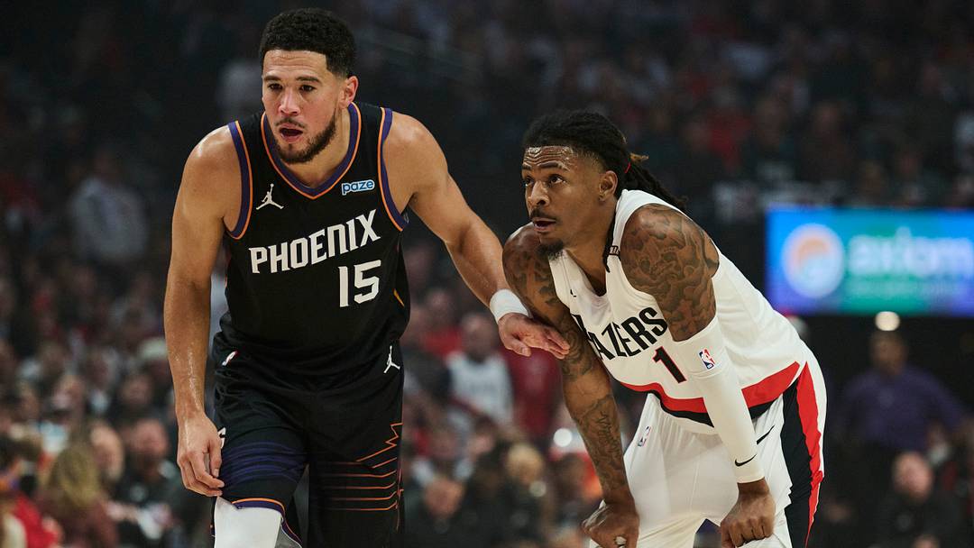 Oct 21, 2026; Portland, Oregon, USA; Phoenix Suns guard Devin Booker (15) holds back Portland Trail Blazers guard Ja Morant (1) during the first half at Moda Center. Mandatory Credit: Troy Wayrynen-Imagn Images