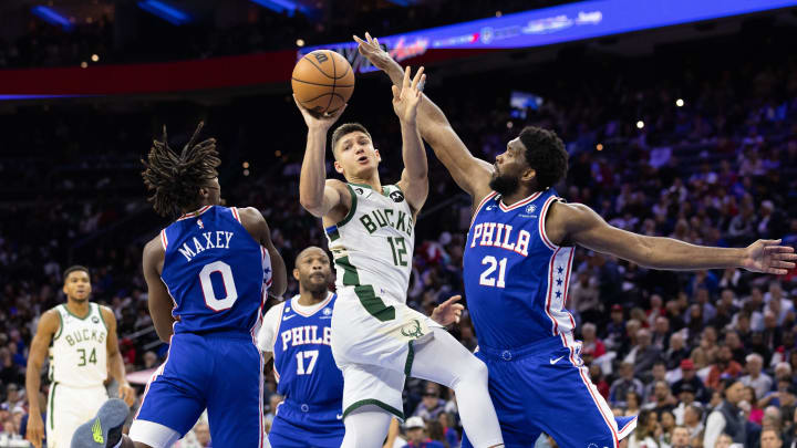 Oct 20, 2022; Philadelphia, Pennsylvania, USA; Milwaukee Bucks guard Grayson Allen (12) passes the ball between Philadelphia 76ers center Joel Embiid (21) and guard Tyrese Maxey (0) during the third quarter at Wells Fargo Center. Mandatory Credit: Bill Streicher-USA TODAY Sports