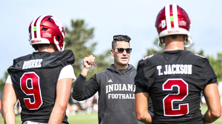 Indiana quarterbacks Kurtis Rourke (9) and Tayven Jackson (2) are given instructions by Indiana quarterbacks coach and co-offensive coordinator Tino Sunseri on July 31, 2024. Indiana quarterbacks Kurtis Rourke (9) and Tayven Jackson (2) are given instructions by Indiana quarterbacks coach and co-offensive coordinator Tino Sunseri on July 31, 2024.