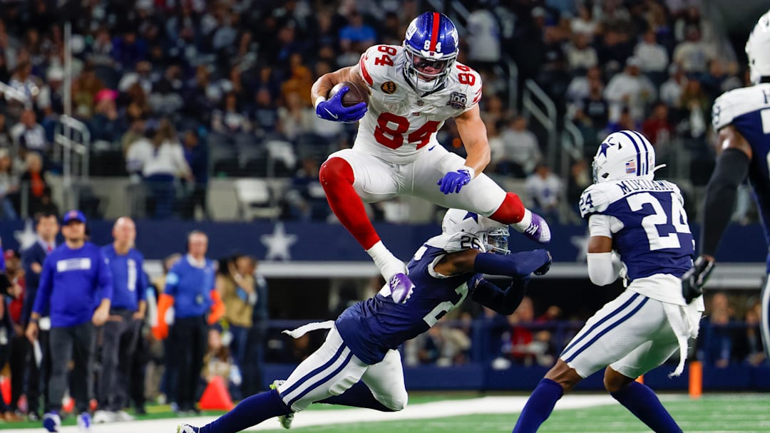 Nov 28, 2024; Arlington, Texas, USA; New York Giants tight end Theo Johnson (84) leaps over Dallas Cowboys cornerback DaRon Bland (26) during the fourth quarter at AT&T Stadium. Mandatory Credit: Andrew Dieb-Imagn Images
