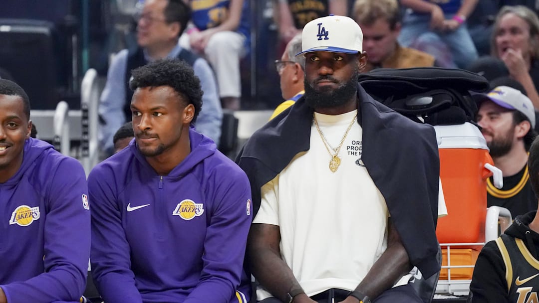 Oct 5, 2025; San Francisco, California, USA;   Los Angeles Lakers guard Bronny James (9) and forward LeBron James (23), wearing a Los Angeles Dodgers cap, watch the action against the Golden State Warriors in the first quarter at Chase Center. Mandatory Credit: David Gonzales-Imagn Images