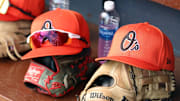 Mar 11, 2024; Tampa, Florida, USA;  A detailed view of Baltimore Orioles baseball hats and gloves in the dugout during the first inning against the New York Yankees at George M. Steinbrenner Field.