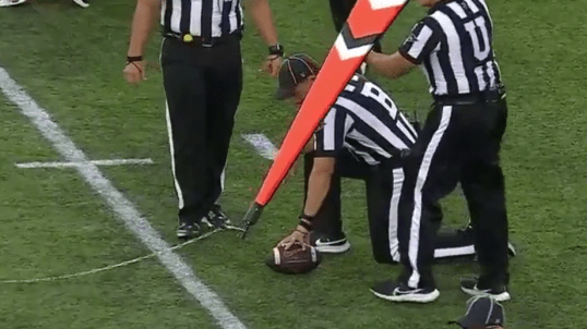SEC officials measure a spot on the field during a college football game.