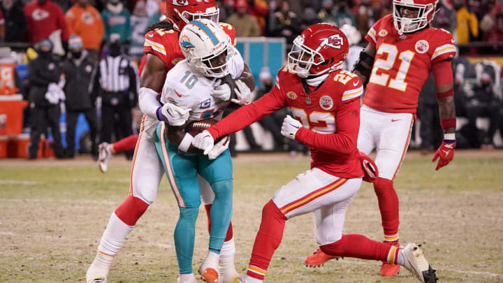 Dolphins wide receiver Tyreek Hill is stopped by Kansas City Chiefs linebacker Nick Bolton (32) as cornerback Trent McDuffie (22) tries to punch the football from his grasp in the 2024 AFC wild card game at GEHA Field at Arrowhead Stadium.
