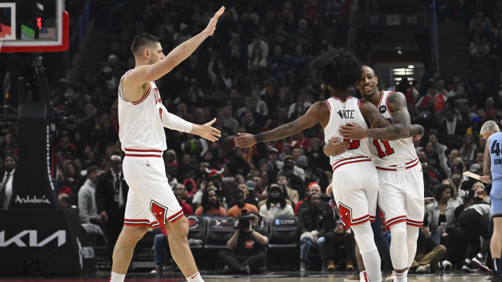 Jan 20, 2024; Chicago, Illinois, USA;  Chicago Bulls forward DeMar DeRozan (11) hugs guard Coby White (0) as center Nikola Vucevic (9) looks on against the Memphis Grizzlies during the second half at the United Center. Mandatory Credit: Matt Marton-USA TODAY Sports