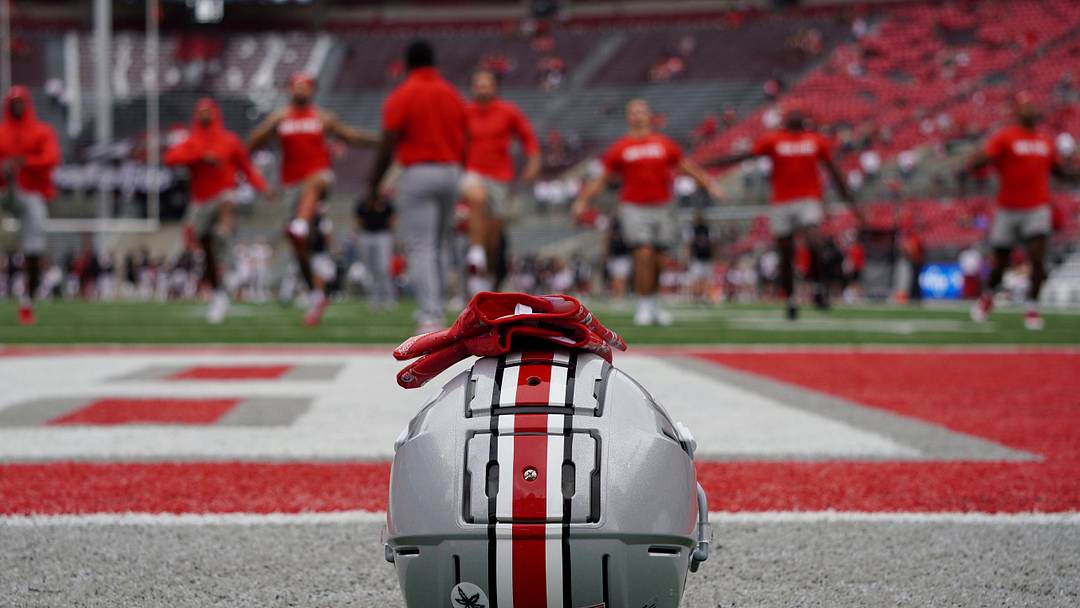 An Ohio State football helmet next to the field at Ohio State while Buckeyes football players warm up.