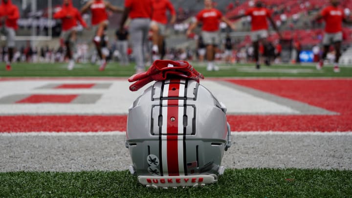 An Ohio State football helmet next to the field at Ohio State while Buckeyes football players warm up.