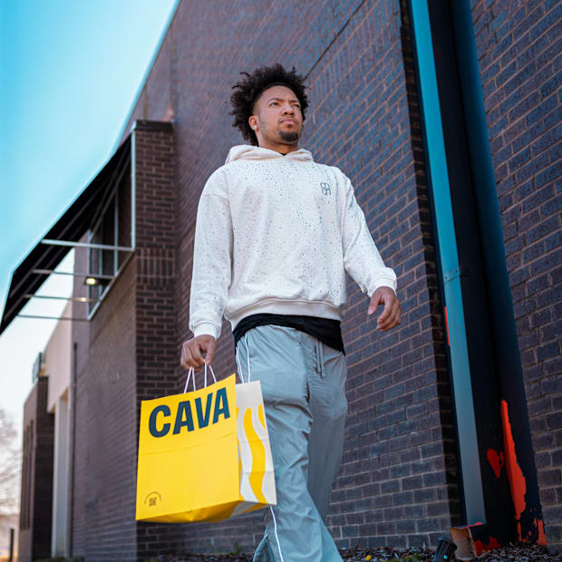 Alabama Crimson Tide college basketball player Mark Sears walks with CAVA yellow food bag wearing grey hoodie and sweats.