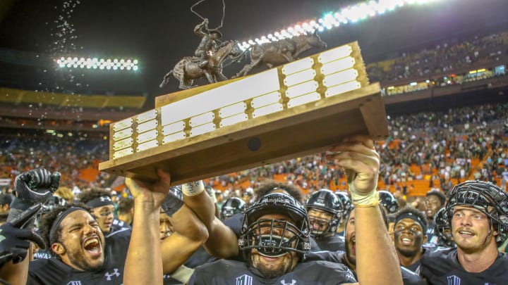 Taaga Tuulima #63 of the Hawaii Rainbow Warriors hoists the 'Paniolo Trophy' as his teammates celebrate the win over the Wyoming Cowboys at Aloha Stadium on October 06, 2018 in Honolulu, Hawaii.