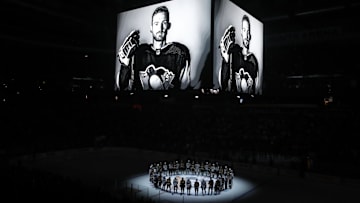 Oct 30, 2023; Pittsburgh, Pennsylvania, USA;  Members of the Anaheim Ducks and the Pittsburgh Penguins stand at center ice for a moment of silence at the PPG Paints Arena to honor former Penguin forward Adam Johnson (on scoreboard) who was tragically killed in a hockey related accident in Europe. Mandatory Credit: Charles LeClaire-Imagn Images