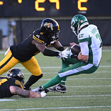 Jun 16, 2024; Hamilton, Ontario, CAN; Saskatchewan Rough Riders quarterback Trevor Harris is tackled by Hamilton Tiger Cats linebacker Ray Wilborn (0) and defensive tackle Casey Sayles (44) in the second quarter at Tim Hortons Field. Mandatory Credit: Gerry Angus-Imagn Images