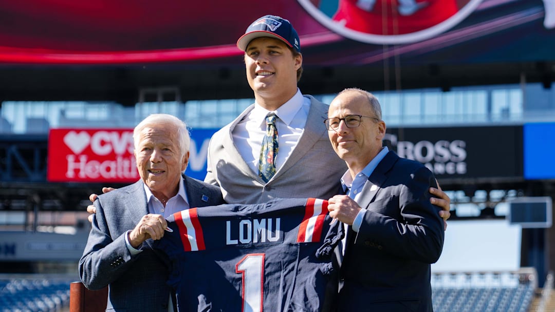 May 7, 2026; Foxborough, MA, USA; New England Patriots first round draft pick Caleb Lomu is presented with a ceremonial first round jersey by team owner Robert Kraft (l) and team president Jonathan Kraft (r) at a press conference on the game field at Gillette Stadium. Mandatory Credit: Natalie Reid-Imagn Images