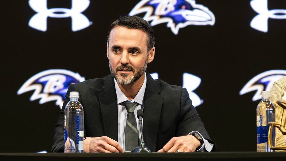 Jesse Minter sits at a Ravens podium in a suit.