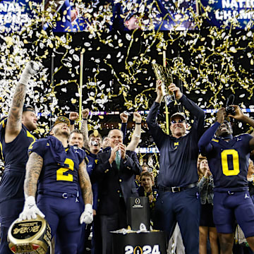 Michigan head coach Jim Harbaugh lifts up the trophy as players and coaches celebrate after 34-13 win over Washington 