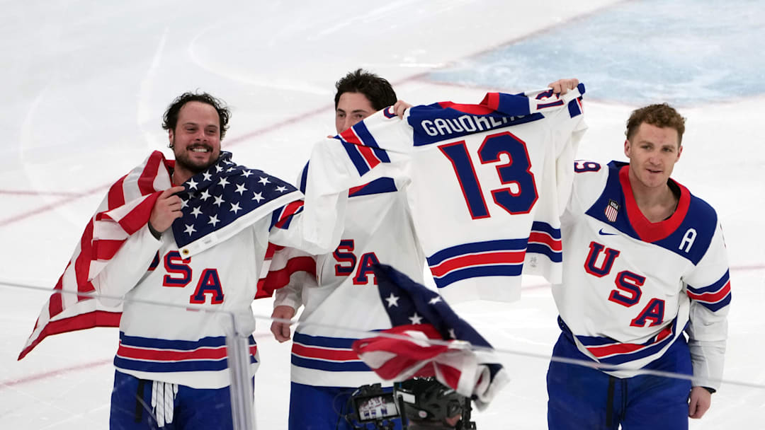 Feb 22, 2026; Milan, Italy; Auston Matthews (left), Zach Werenski (center) and Matthew Tkachuk (right) of the United States hold the jersey of the late Johnny Gaudreau after winning the men's ice hockey gold medal game during the Milano Cortina 2026 Olympic Winter Games at Milano Santagiulia Ice Hockey Arena. Mandatory Credit: James Lang-Imagn Images

