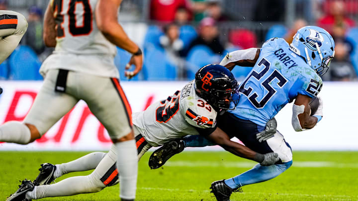 Jun 9, 2024; Toronto, Ontario, CAN; BC Lions defensive back Emmanuel Rugamba (33) tackles Toronto Argonauts running back Ka'Deem Carey (25) at BMO Field. Mandatory Credit: Kevin Sousa-Imagn Images