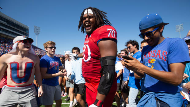 Kansas redshirt sophomore offensive lineman Kobe Baynes (70) celebrates with fans as they run on to the field Saturday after 