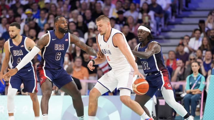 Jul 28, 2024; Villeneuve-d'Ascq, France; Serbia power forward Nikola Jokic (15) dribbles against United States guard Lebron James (6) and guard Jrue Holiday (12) in the first quarter during the Paris 2024 Olympic Summer Games at Stade Pierre-Mauroy.