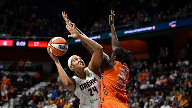 Two basketball players in white and orange uniforms while one player looks up to shoot an orange and white basketball.