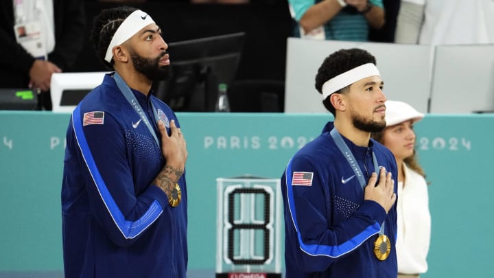 Aug 10, 2024; Paris, France; United States guard Devin Booker (15) and centre Anthony Davis (14) listen to the national anthem on the podium after defeating France in the men's basketball gold medal game during the Paris 2024 Olympic Summer Games at Accor Arena. Mandatory Credit: Rob Schumacher-USA TODAY Sports