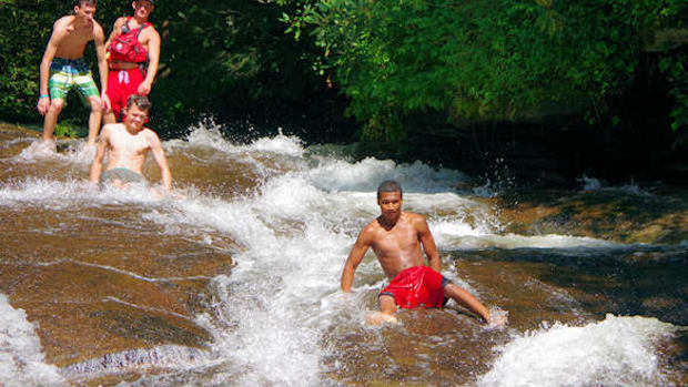 Two men sliding down a natural water slide called Sliding Rock in North Carolina.