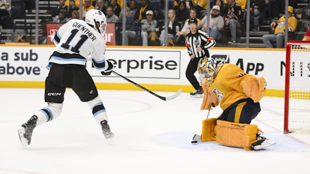 Hockey goalie in yellow uniform stops shot attempt from player in white unifor