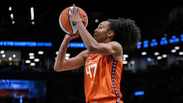 Connecticut Sun guard Leila Lacan shoots the ball during a game, wearing an orange jersey with black and purple borders.