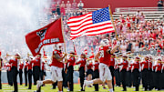 Sep 6, 2025; Raleigh, North Carolina, USA; North Carolina State Wolfpack defensive end Colby Cronk (58) runs with the American flag while defensive lineman Joseph Castaneda (97) runs with North Carolina State Wolfpack flag before the first half of the game against the Virginia Cavaliers at Carter-Finley Stadium. Mandatory Credit: Jaylynn Nash-Imagn Images