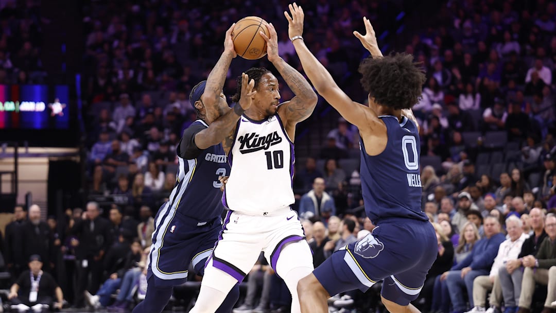 Nov 30, 2025; Sacramento, California, USA; Sacramento Kings forward/guard DeMar DeRozan (10) controls the ball between Memphis Grizzlies guard Kentavious Caldwell-Pope (3) and forward Jaylen Wells (0) during the third quarter at Golden 1 Center. Mandatory Credit: Kelley L Cox-Imagn Images