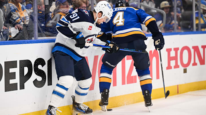May 2, 2025; St. Louis, Missouri,  USA; Winnipeg Jets center Cole Perfetti (91) and St. Louis Blues defenseman Nick Leddy (4) battle for a loose puck during the first period in game six of the first round of the 2025 Stanley Cup Playoffs at Enterprise Center. Mandatory Credit: Connor Hamilton-Imagn Images