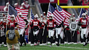 Nov 8, 2025; Madison, Wisconsin, USA;  Wisconsin Badgers players carry American flags while jogging onto the field prior to the game against the Washington Huskies at Camp Randall Stadium. Mandatory Credit: Jeff Hanisch-Imagn Images