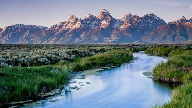 A stream running through green lucious grass with beautiful mountains in the background.