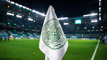 Detailed shot of a corner flag with the Celtic Glasgow coat of arms, illuminated stadium in the background. 