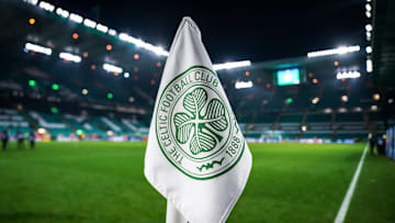 Detailed shot of a corner flag with the Celtic Glasgow coat of arms, illuminated stadium in the background. 