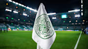 Detailed shot of a corner flag with the Celtic Glasgow coat of arms, illuminated stadium in the background. 