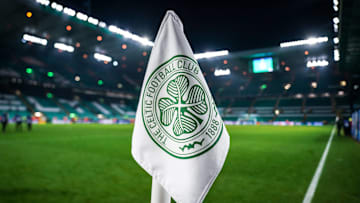 Detailed shot of a corner flag with the Celtic Glasgow coat of arms, illuminated stadium in the background. 