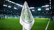 Detailed shot of a corner flag with the Celtic Glasgow coat of arms, illuminated stadium in the background. 