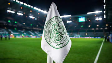 Detailed shot of a corner flag with the Celtic Glasgow coat of arms, illuminated stadium in the background. 