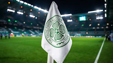 Detailed shot of a corner flag with the Celtic Glasgow coat of arms, illuminated stadium in the background. 