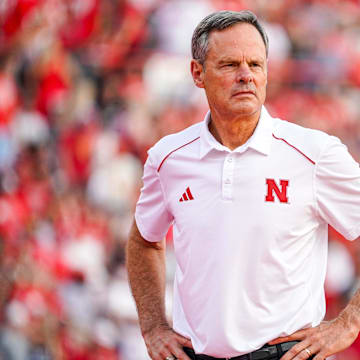 Nebraska volleyball head coach John Cook stands on the court at Memorial Stadium wearing a white polo and black pants.