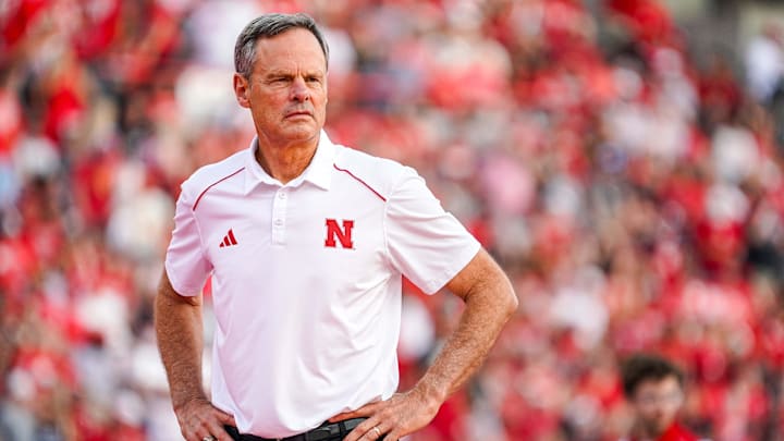 Nebraska volleyball head coach John Cook stands on the court at Memorial Stadium wearing a white polo and black pants.