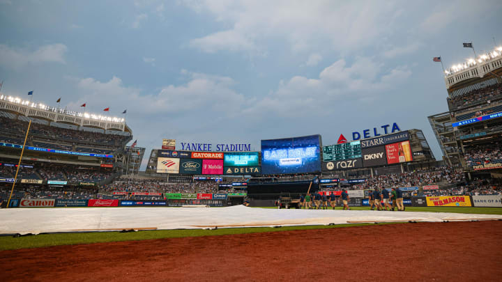 Jul 5, 2024; Bronx, New York, USA; A rain delay message is displayed on the main scoreboard as Yankees ground crew cover the field with a tarp. Mandatory Credit: Vincent Carchietta-USA TODAY Sports