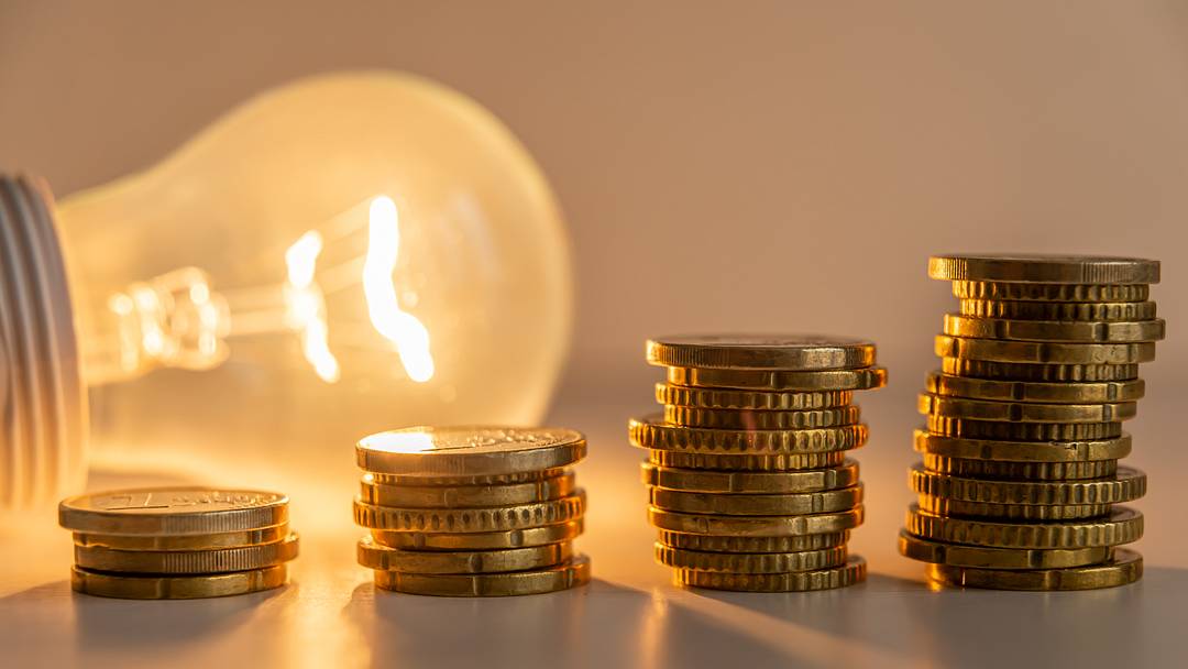 Lit light bulb with coins beside it. Lit light bulb with coins beside it.